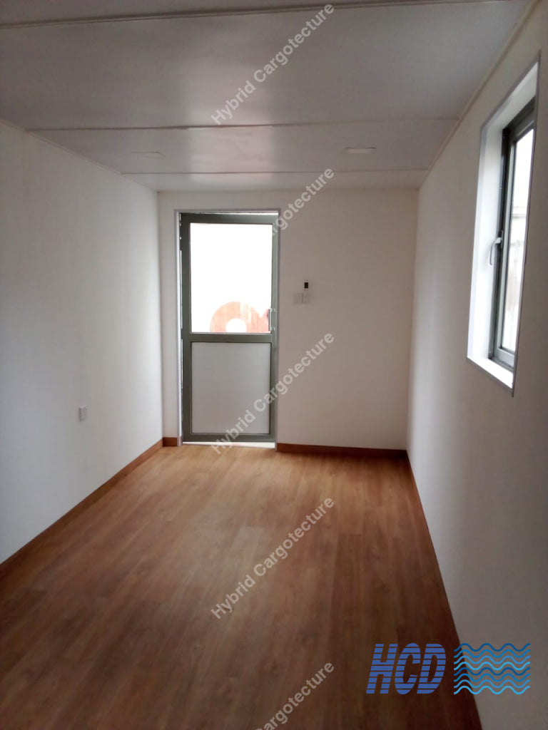 An empty room with light-colored walls, a brown wood-look laminate floor, a white ceiling, a glass door at the back, and a window on the right wall.