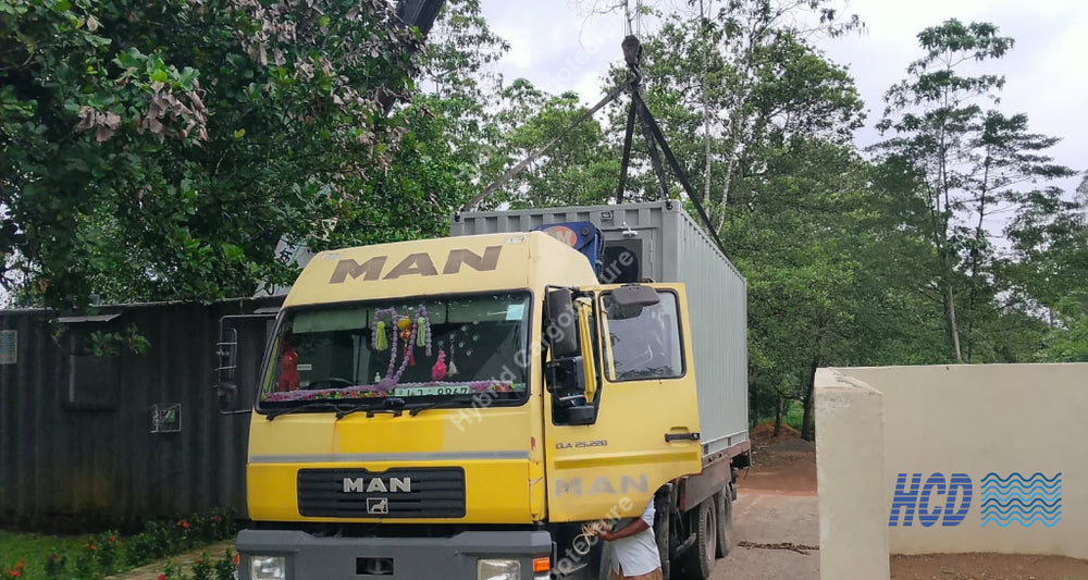 A yellow MAN box truck parked outdoors in front of trees and a building, with a crane arm visible above the cargo container.