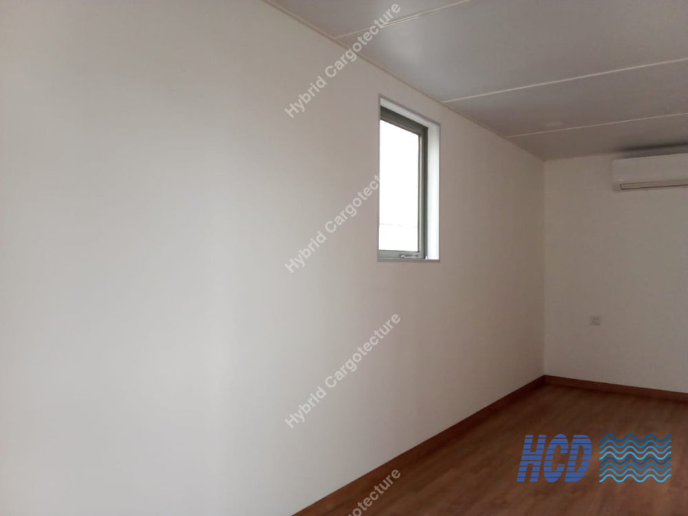 An empty room with off-white walls, a small window, a white ceiling, and brown wood flooring.