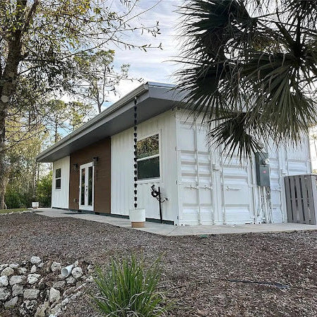 Modern house with a white exterior and brown accents, surrounded by trees and shrubs.