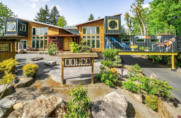 Modern house with a unique design featuring shipping containers, surrounded by greenery.