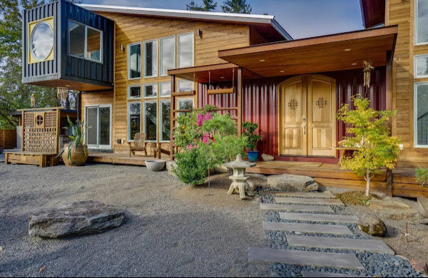 Modern wooden house with a patio area featuring plants and a stone pathway.