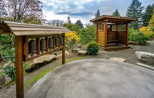 Traditional wooden bell tower and pavilion in a garden setting with trees and rocks.
