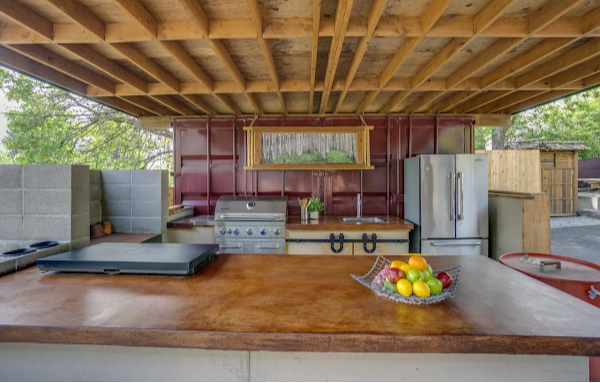 Outdoor kitchen with wooden counter, grill, refrigerator, and fruit bowl.