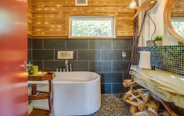 Bathroom with freestanding bathtub, wooden walls, and a window.