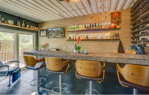 Modern bar area with wooden counter, stools, and shelves with bottles.