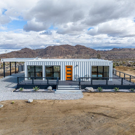 Modern house made from shipping containers in a desert landscape with mountains in the background.