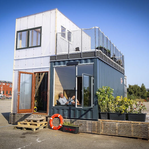 Modular building with a rooftop deck and plants, set against a clear blue sky.