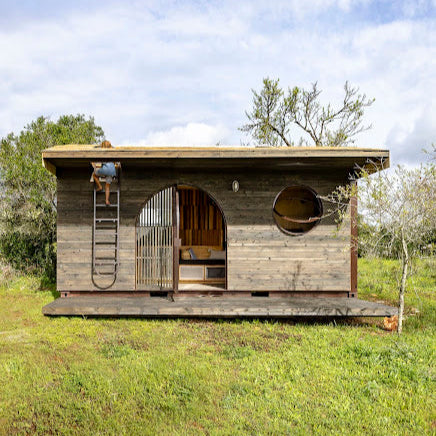 Wooden cabin in a grassy field with trees in the background