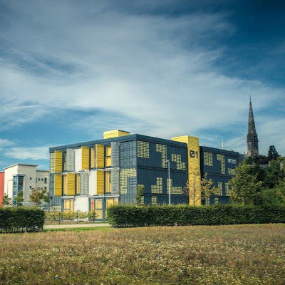 Modern building with colorful facade in a park-like setting with a church spire in the background
