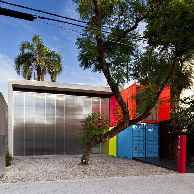 Modern building with colorful shipping container design, surrounded by trees and a clear sky.