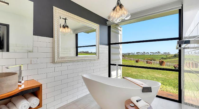 Modern bathroom with a freestanding bathtub, mirror, and view of a green landscape.