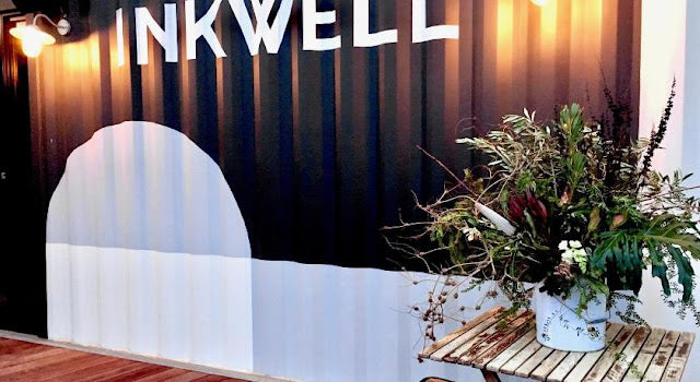 Inkwell branding with a decorative setup featuring plants and a table.