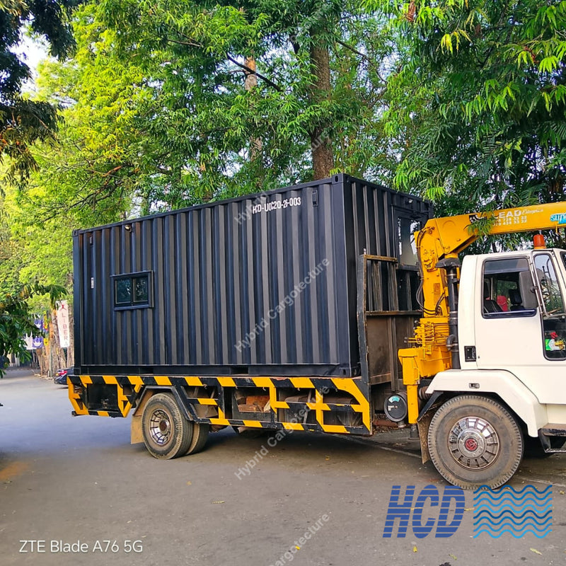 Truck with a crane lifting a black container on a street lined with trees.