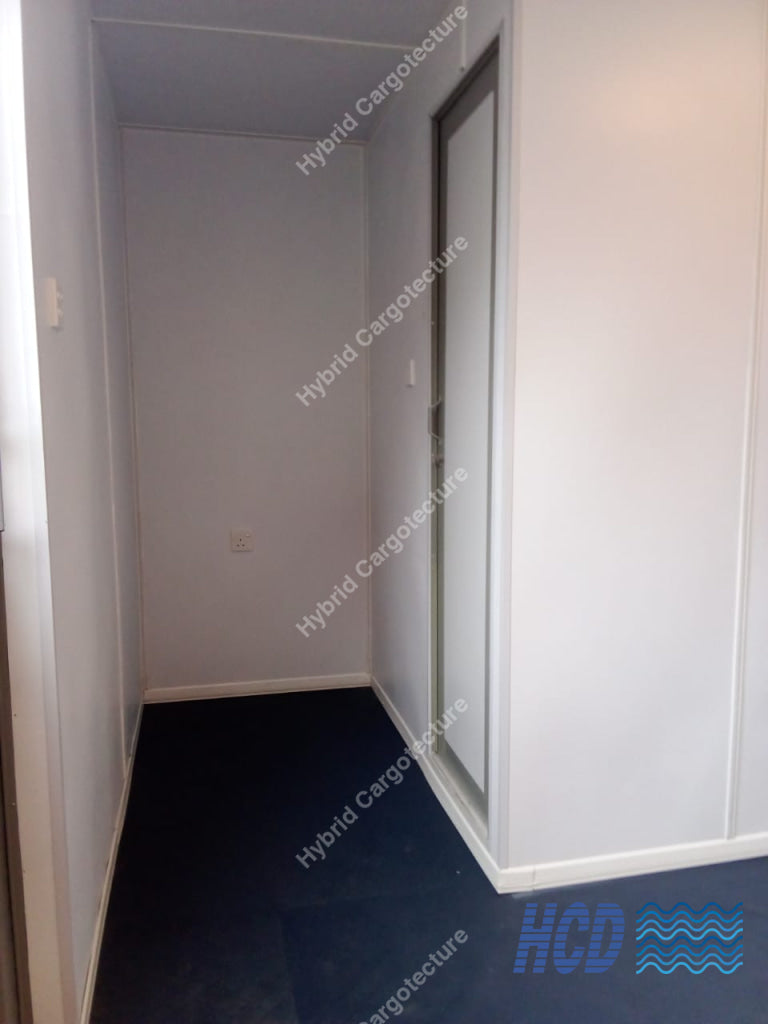 An empty narrow hallway or room corner with white walls, a white door frame, and a dark navy blue carpet on the floor.