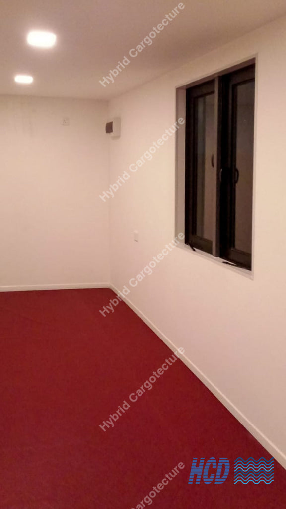 Empty office container room with red carpet and a window on the wall.