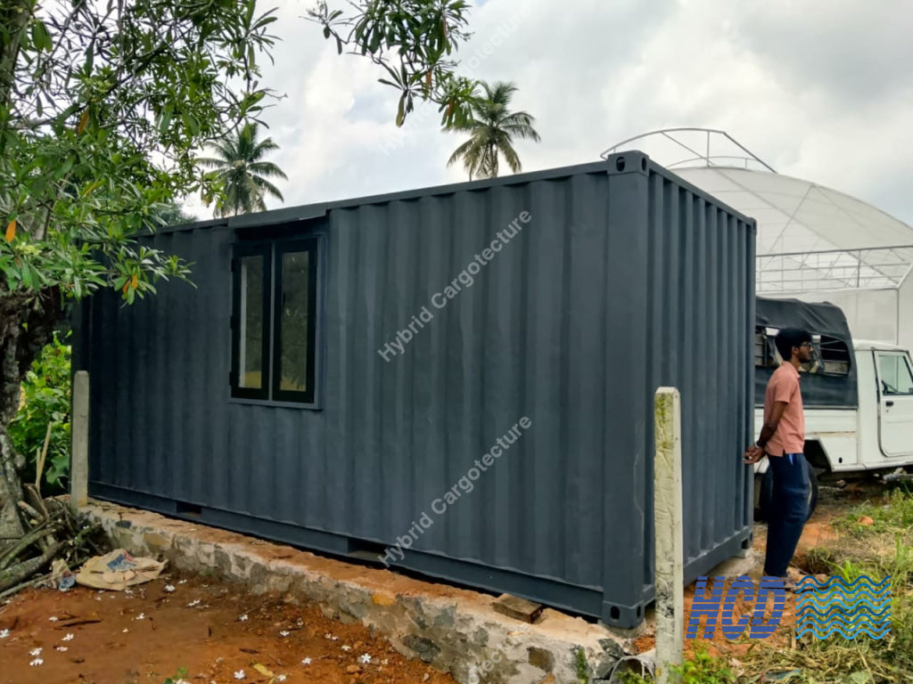 Modular building made from a shipping container in a natural setting with trees and a person standing nearby.