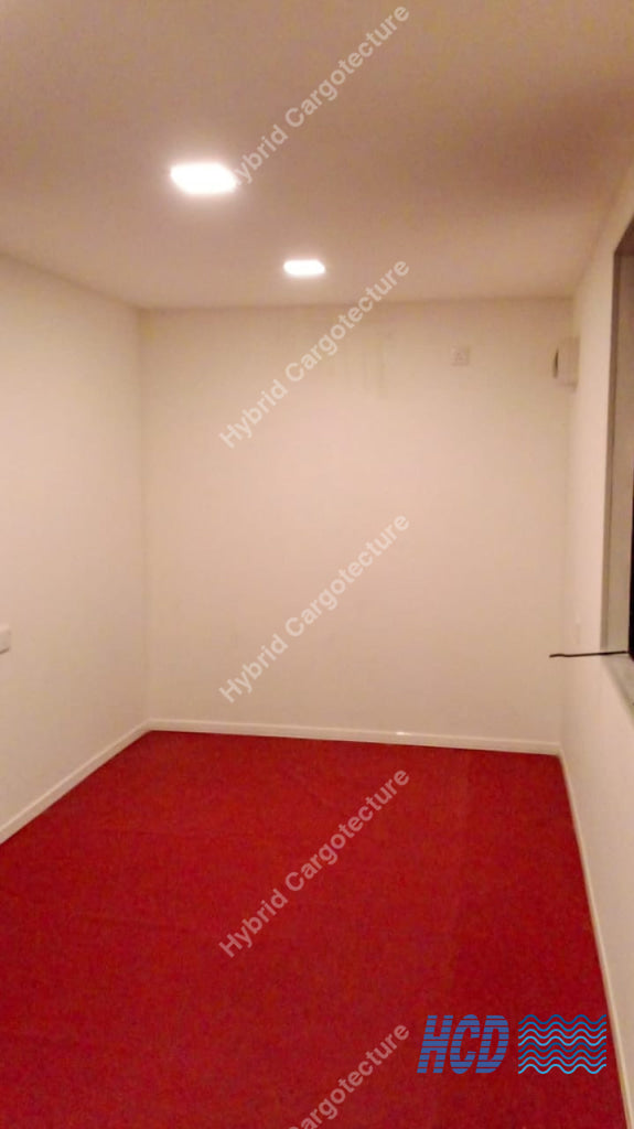 Empty office container room with red carpet, white walls, and recessed lighting.