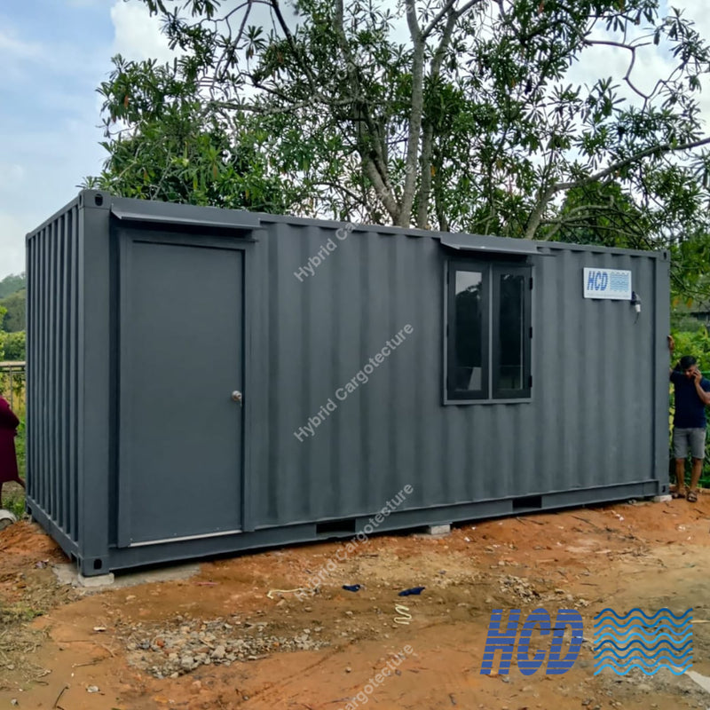 Modular building made from a shipping container on a construction site with trees in the background.