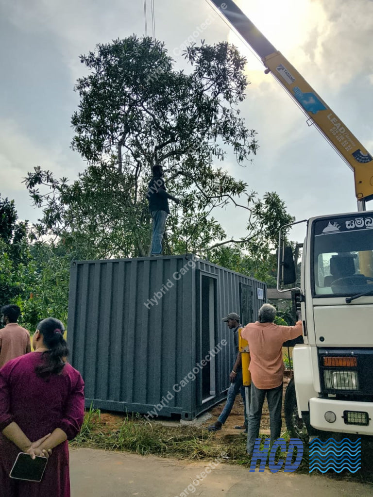 People working around a shipping container with a crane in an outdoor setting