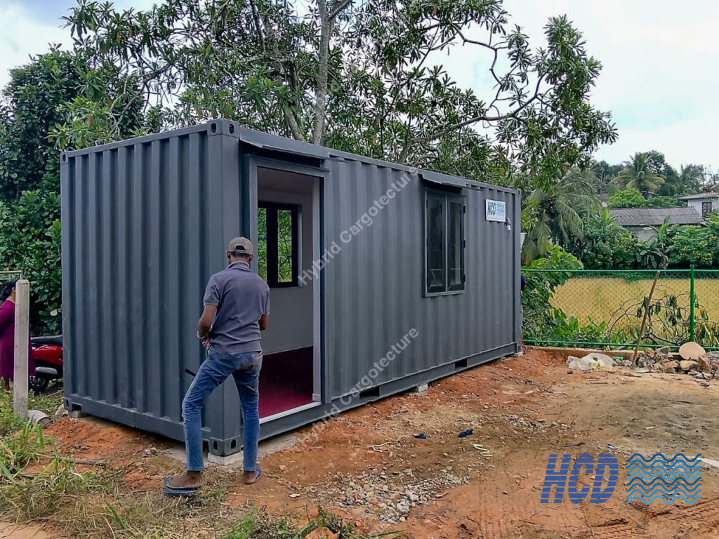 Man standing outside a gray shipping container with trees and open land in the background