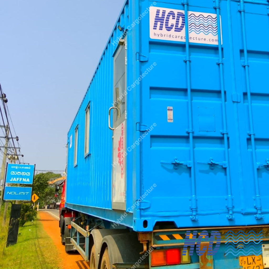Blue shipping container on a truck with 'HCD' branding on a clear day.