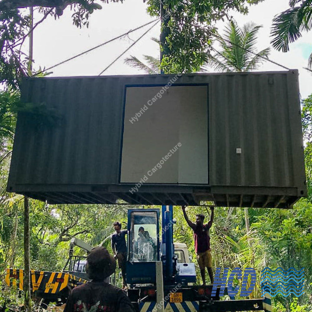 Two people working with a large shipping container in a forested area.