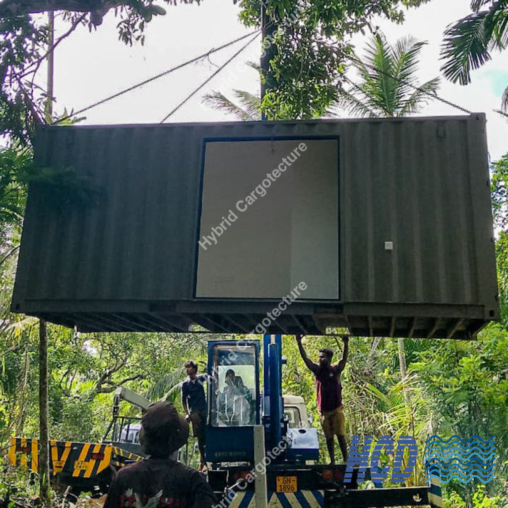 Two people working with a large shipping container in a forested area.